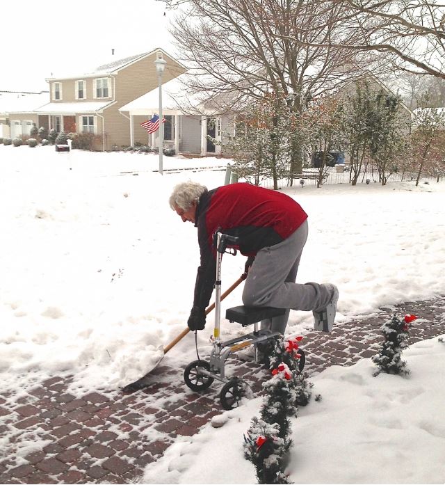 Man shoveling snow on knee scooter