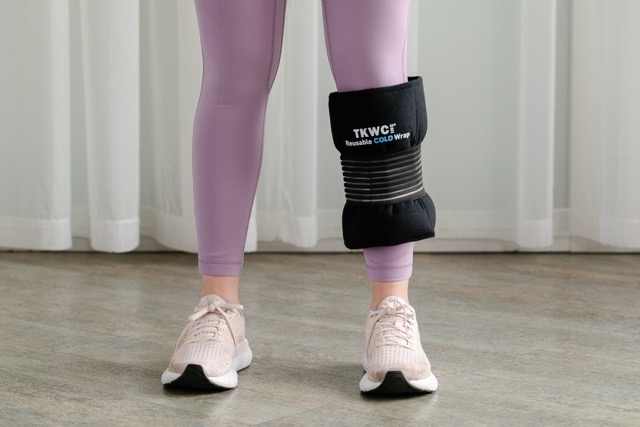 Person wearing light pink sneakers and purple leggings with a black reusable cold wrap labeled 