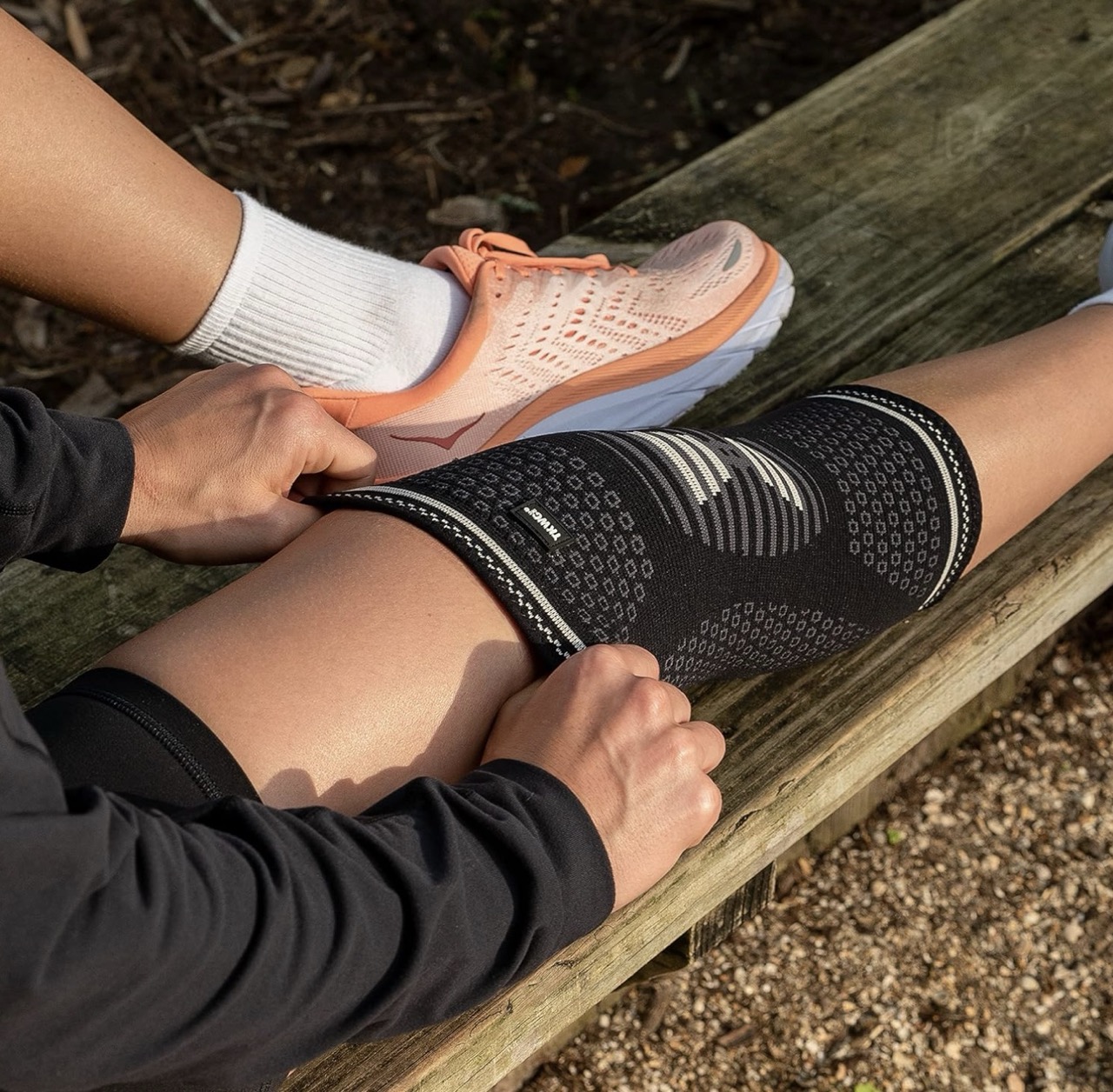 Close-up of hands adjusting a black knee sleeve on a seated leg, showing detailed textured design and silicone grip band.