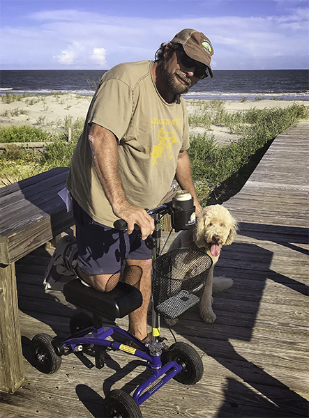 man with knee scooter at beach with dog