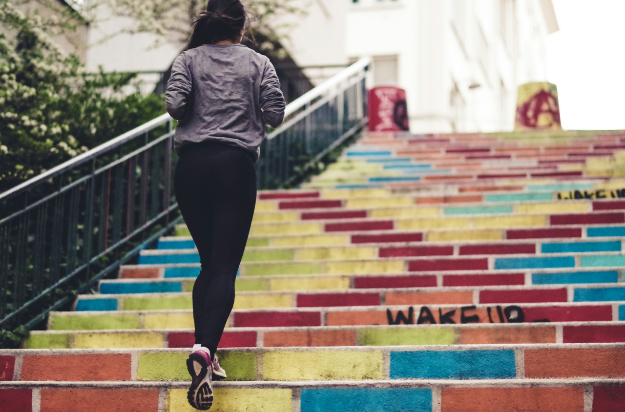 A woman running up colorful, graffiti-covered stairs outdoors, viewed from behind.