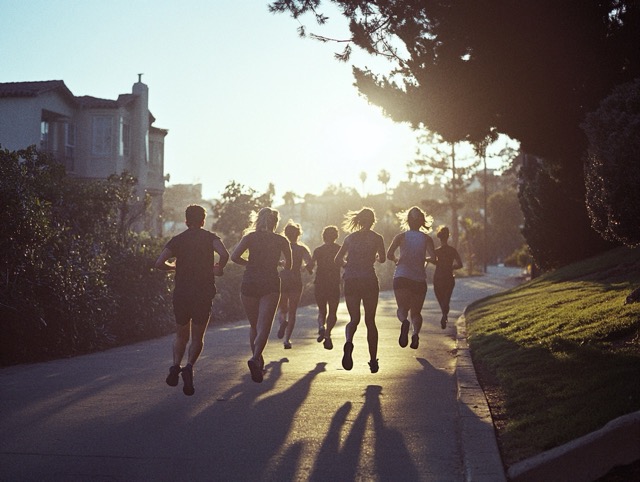 Group of runners on a residential road at sunrise or sunset, their shadows stretching out behind them as they move.