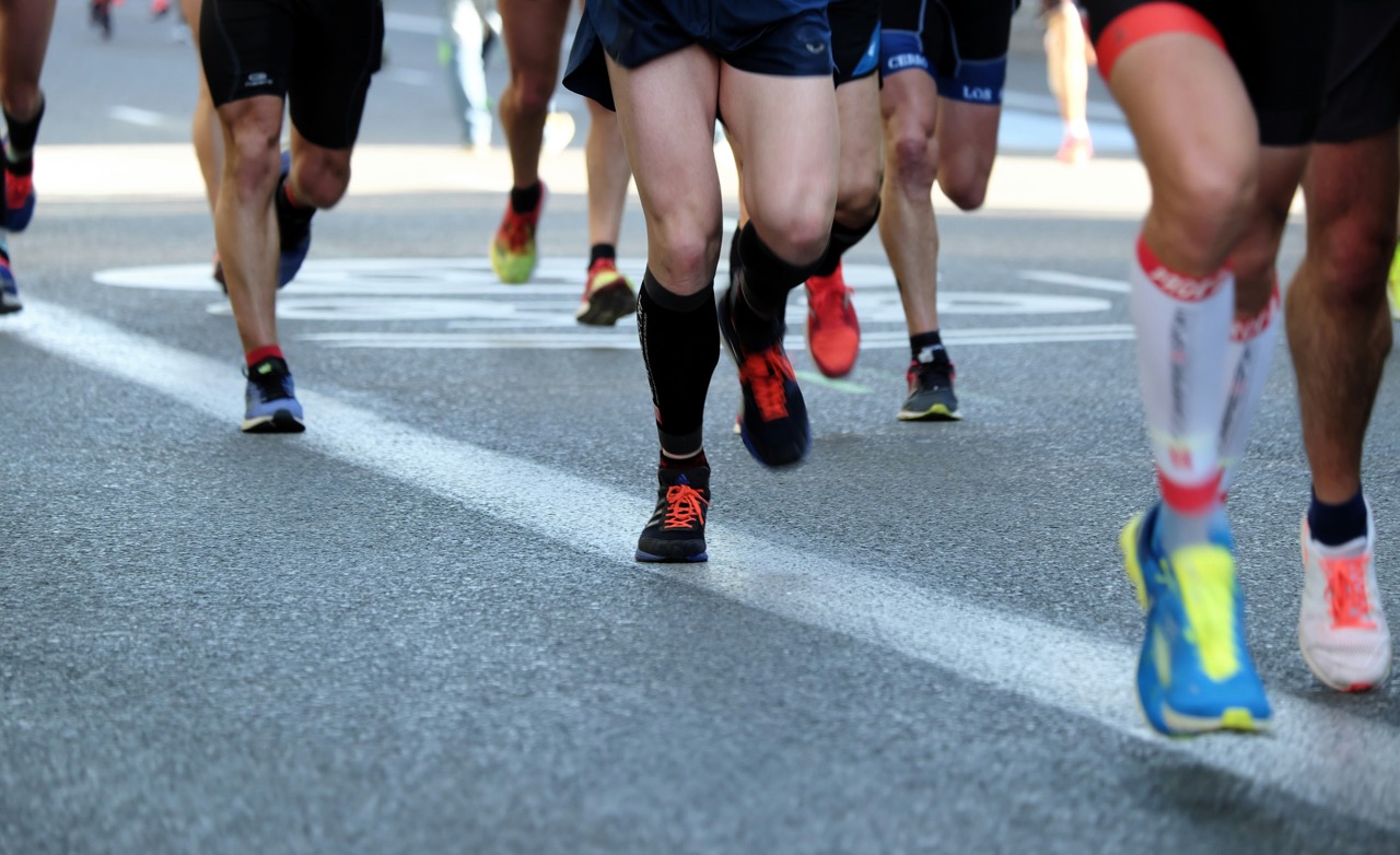 A close-up of runners' legs and shoes on a road during a marathon, showcasing colorful footwear.