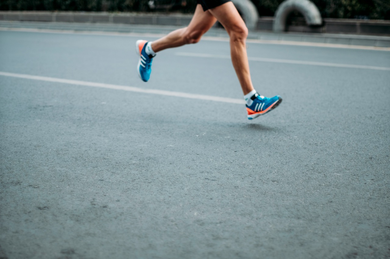 A runner's legs in motion on a road, wearing blue and orange running shoes, captured mid-stride.